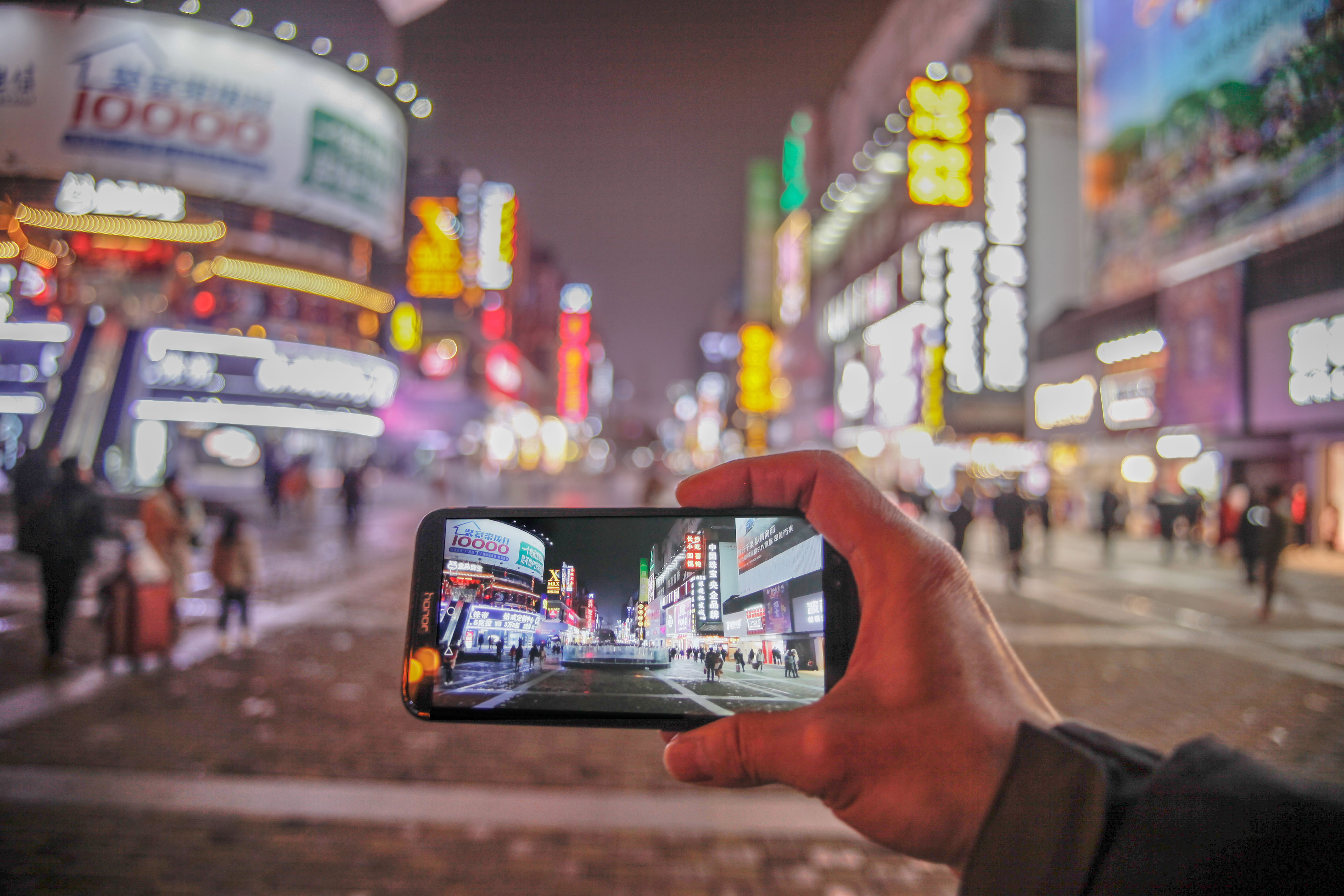 【32号作品：画中画】
手机屏中的步行商业街街景，与虚化的绚烂夜景融为一体，别具一番情趣。